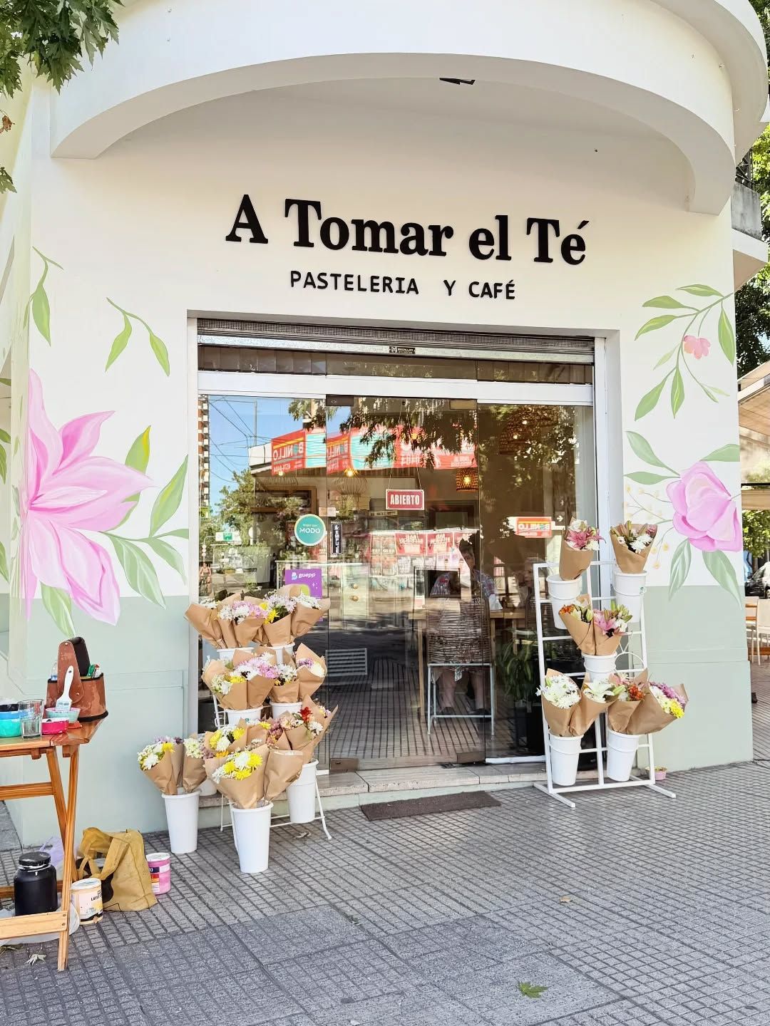 Frente de la pastelería A Tomar el Té con magnolias rosadas y hojas verdes a los dos lados de la puerta.