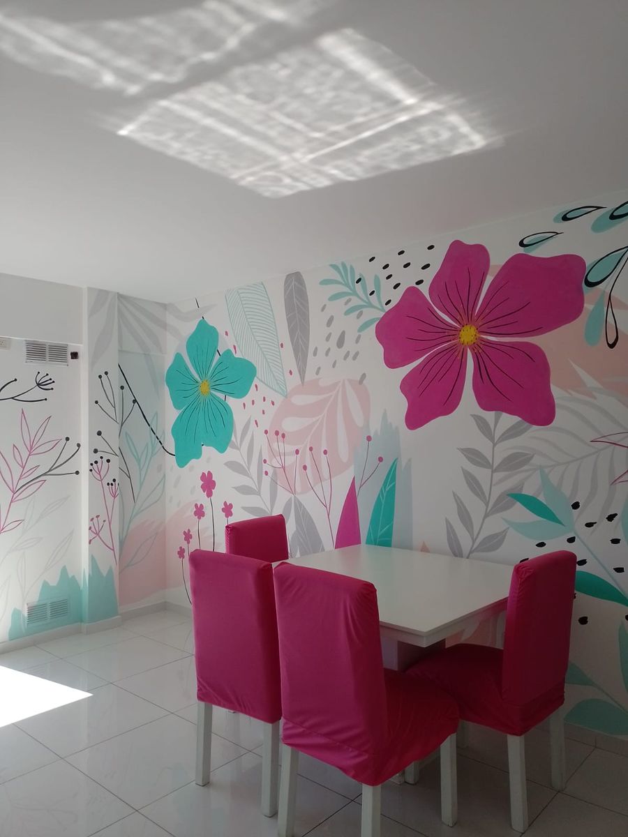 Comedor con sillas fucsia y una pared pintada con una flor fucsia grande, flores turquesa y hojas grises.