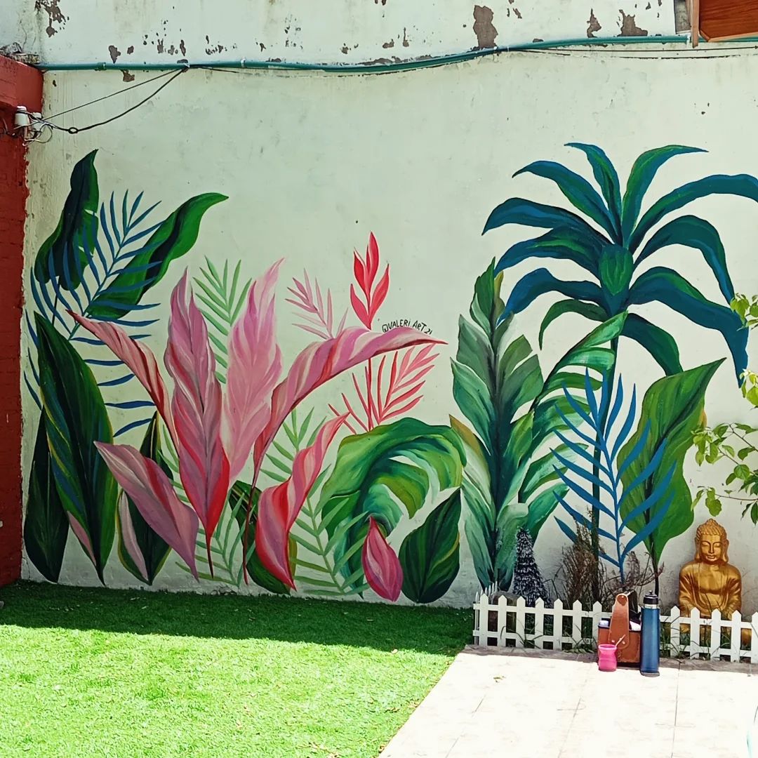 Muro de jardín de Quinta Coquito's con palmeras y plantas de hojas rosas y rojas, detrás de un cerco blanco sobre el pasto.