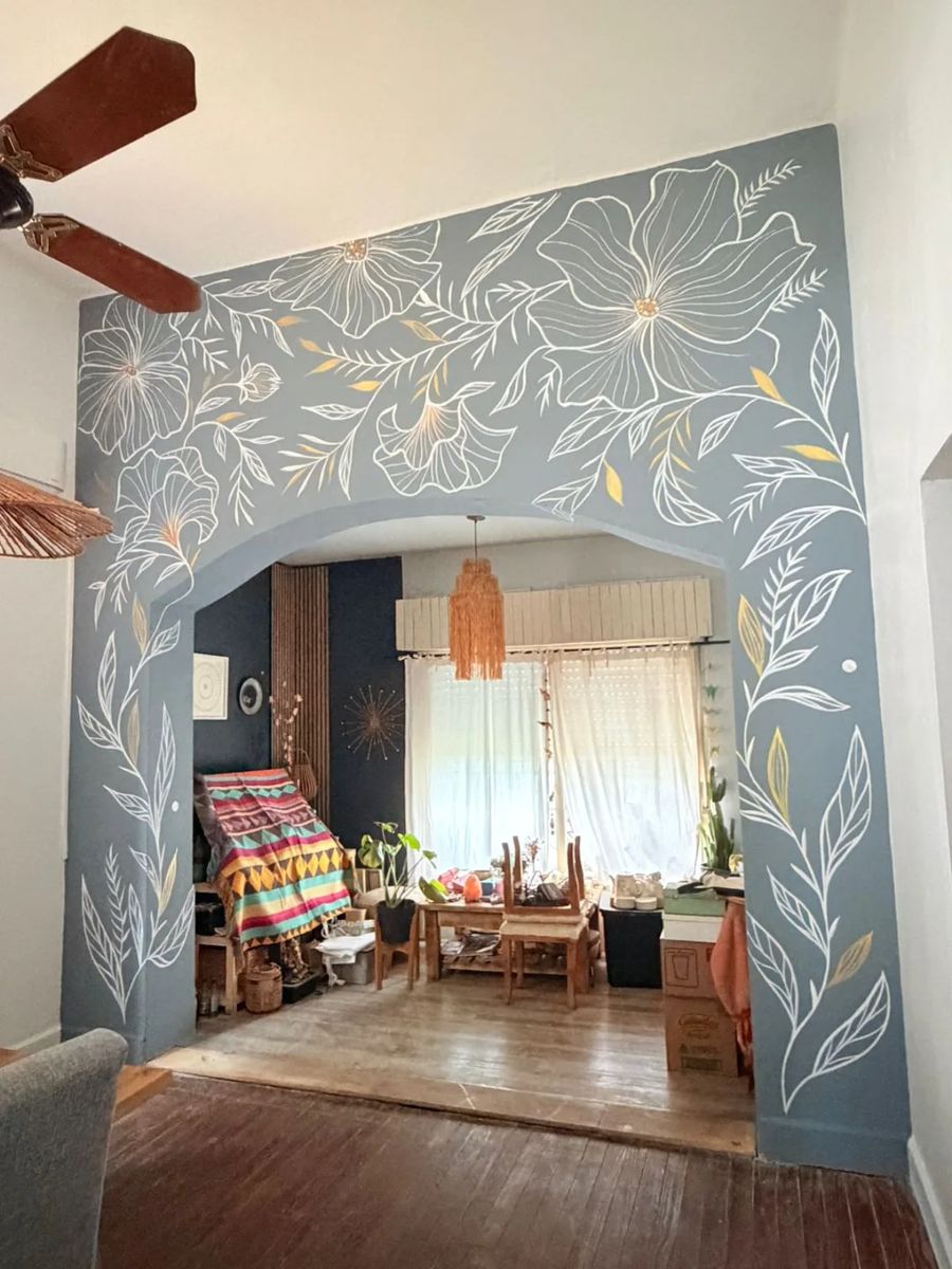 Arco y columnas de una casa pintados de gris con ramas y flores en línea blanca y dorada.