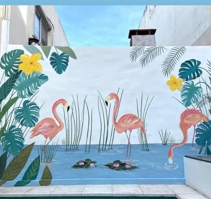 Muro de patio con tres flamencos rosados en un estanque azul, juncos y hojas tropicales.
