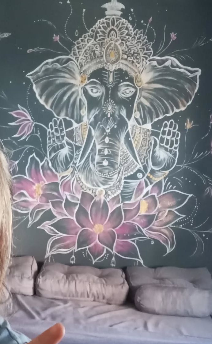 Mural de una figura de Ganesha en línea blanca sobre pared malva, con flor de loto.