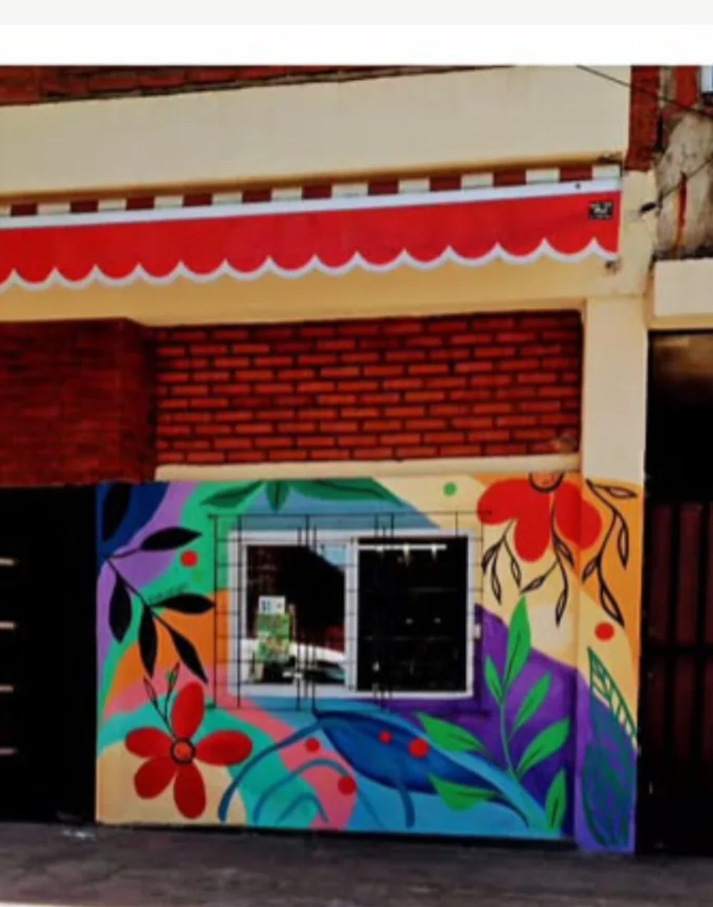 El mismo frente después del mural: flores rojas y hojas violetas sobre la pared y la persiana.