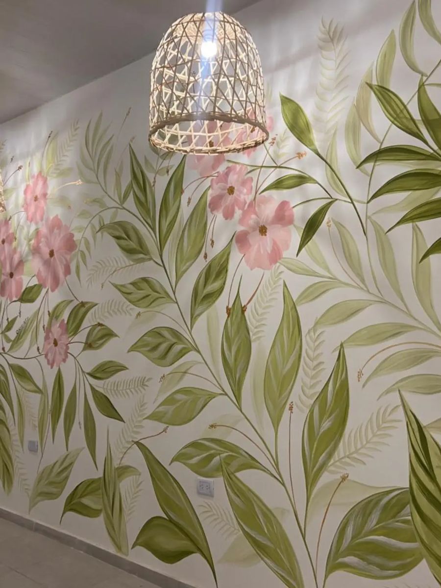 Salón de Loreto Eventos con hojas verdes y flores rosas pintadas sobre la pared blanca, bajo una lámpara de mimbre.