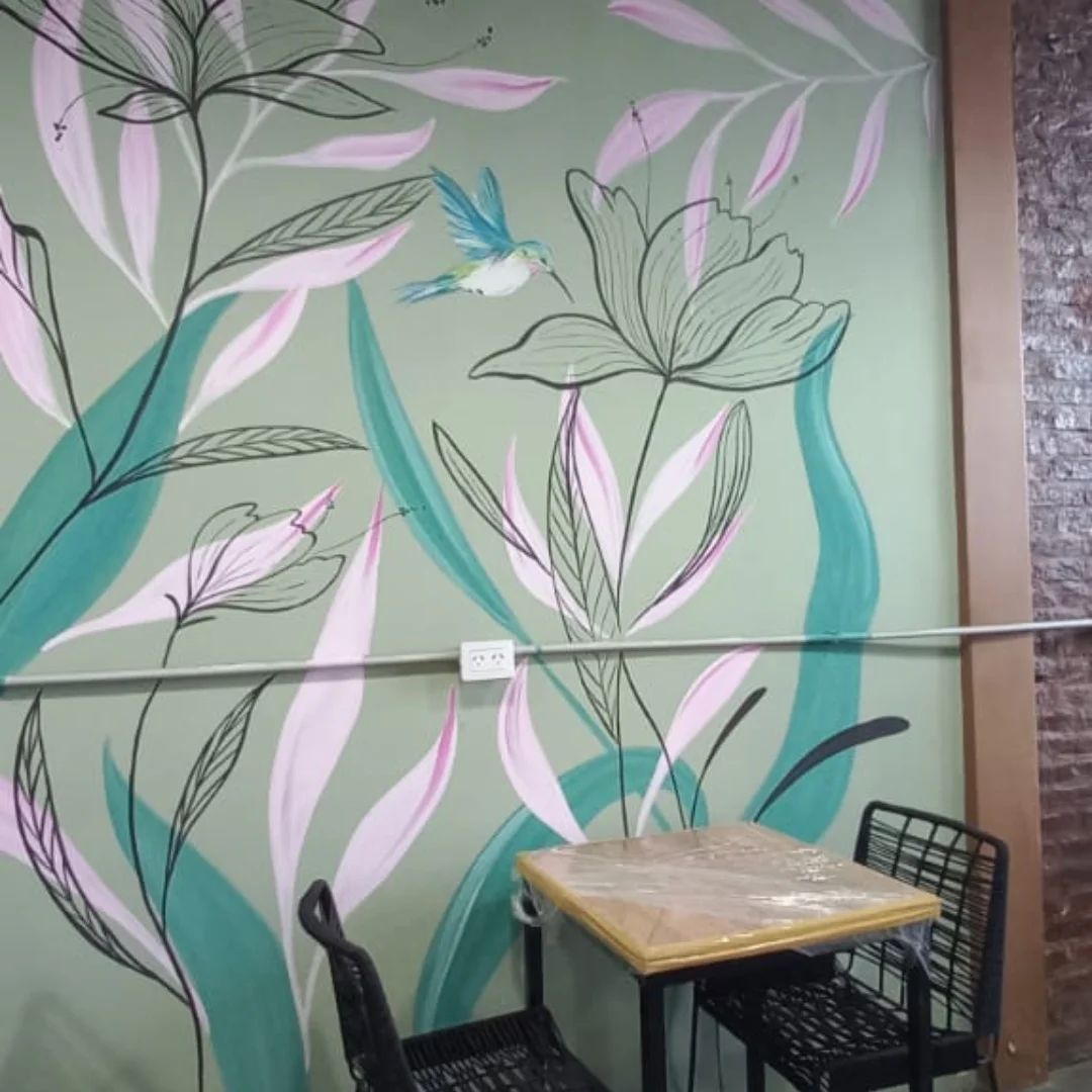 Salón de la panadería Misky con hojas rosas y turquesa y un colibrí pintados sobre la pared verde.