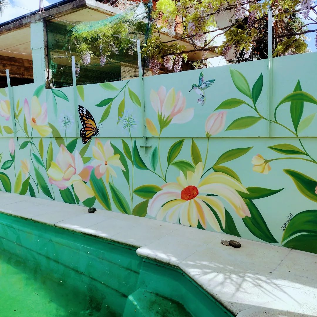 Muro verde agua de una pileta pintado con flores rosas y amarillas, hojas y una mariposa.