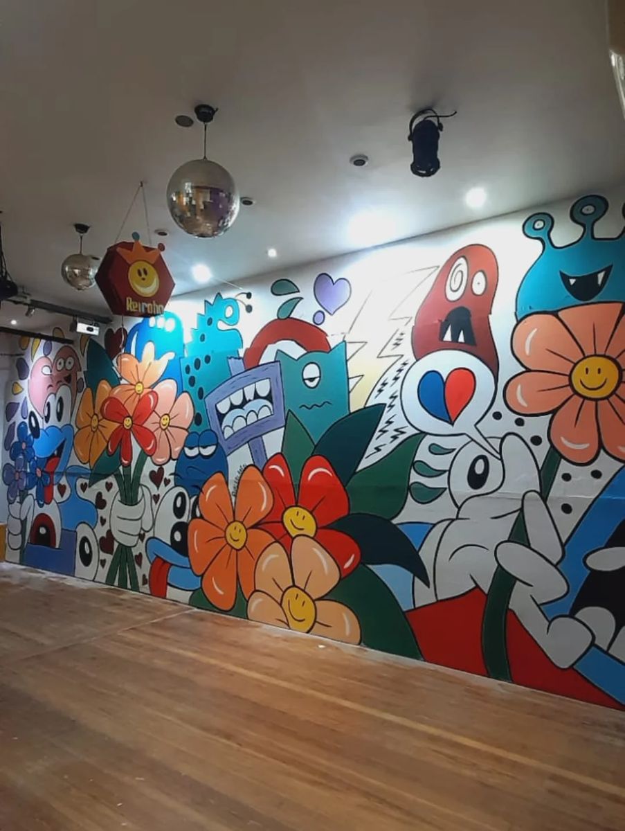 Salón de Reiroho pintado de punta a punta con flores naranjas y rojas, personajes de dibujo azules y corazones.