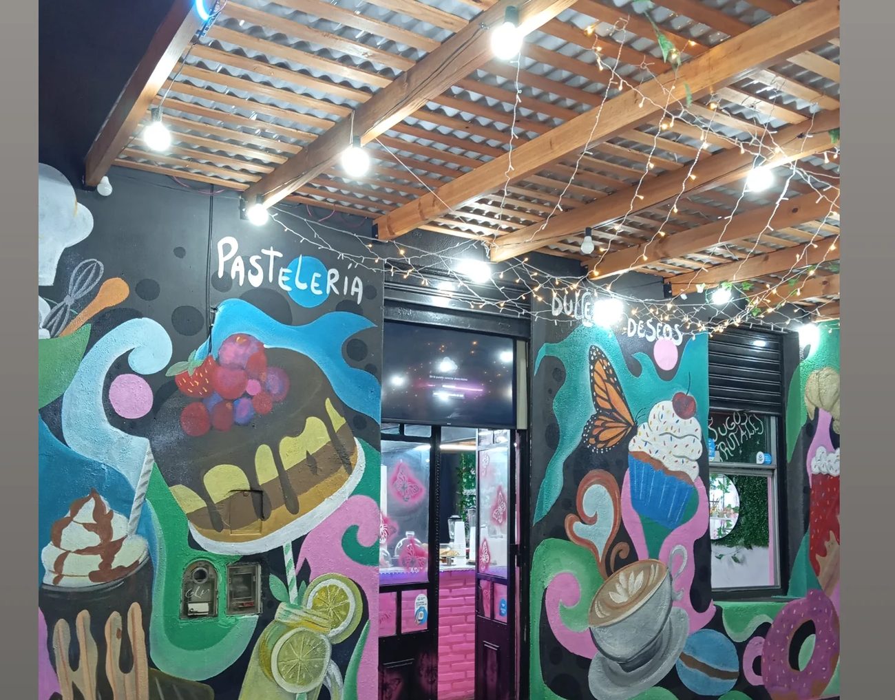 Salón de una pastelería con tortas, helados y frutas pintados en grande sobre la pared.