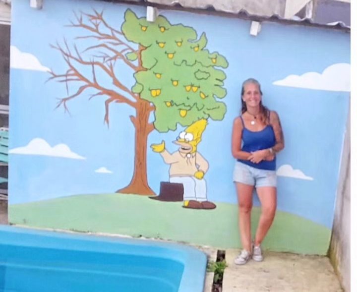Muro junto a una pileta pintado con un árbol, césped y cielo celeste.