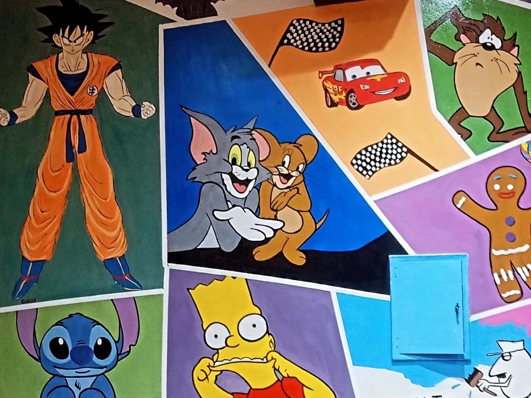 Pared de un local pintada en viñetas de colores con personajes de dibujos animados: Goku, Tom y Jerry, el Rayo McQueen, Stitch y Bart Simpson.