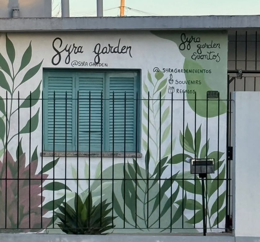 Frente de Syra Garden con plantas y hojas pintadas alrededor de la ventana y la reja.